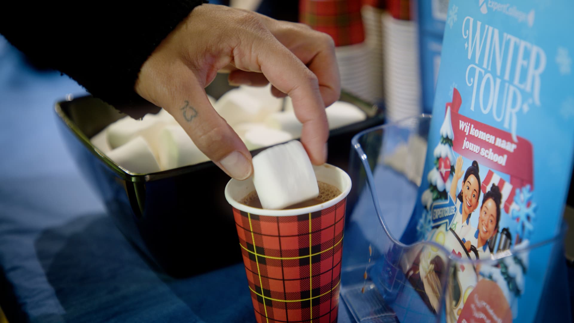 Marshmallow in een beker warme chocolademelk naast de Winter Tour-flyer